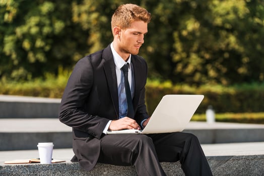 Working outdoors. Confident young man in shirt and tie working on laptop while sitting outdoors photo