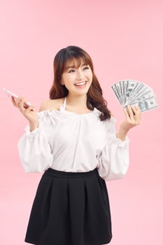 Portrait of young asian woman showing bunch of money banknotes on pink background photo