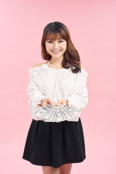 Photo of a happy dreaming young girl isolated over pink wall background holding money.