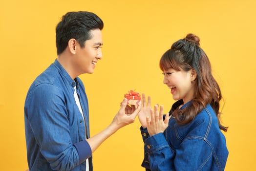 love, couple, proposal and people concept - man giving diamond engagement ring in little red box to happy woman over  yellow background photo