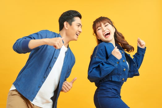 Affectionate interracial couple holding hands and dancing together over yellow background, having fun. photo