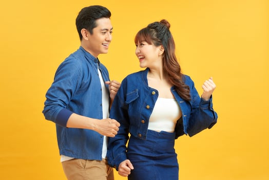 Affectionate interracial couple holding hands and dancing together over yellow background, having fun. photo