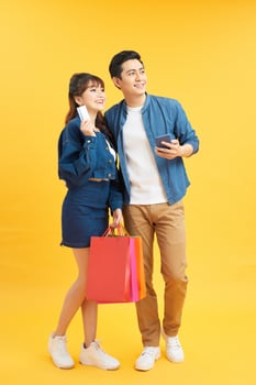 portrait of smiling couple holding shopping bags and credit card isolated on yellow photo