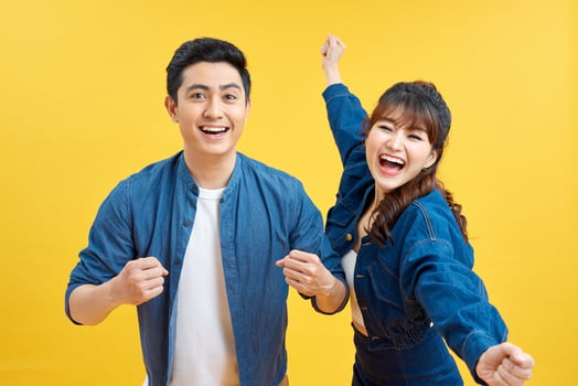 Cheerful couple is celebrating with raised hands, standing on pure background in casual outfits photo