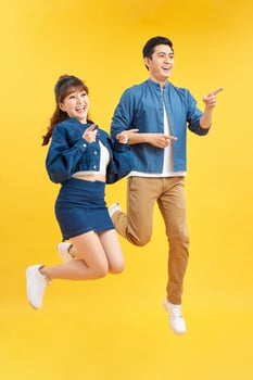 Portrait of funky couple jumping in air holding hands up enjoying time together isolated on yellow background photo