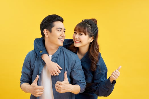 Portrait of smiling couple man and woman showing thumb up together while doing piggyback ride isolated over yellow background photo