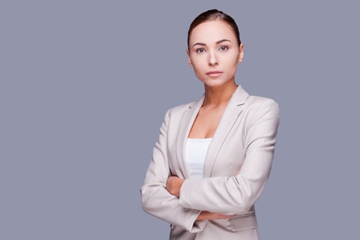 Confident businesswoman. Confident young businesswoman keeping arms crossed while standing against grey background photo