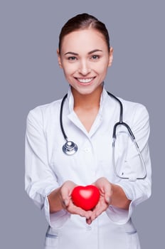 Your heart in good hands. Confident female doctor in white uniform holding heart prop and smiling photo