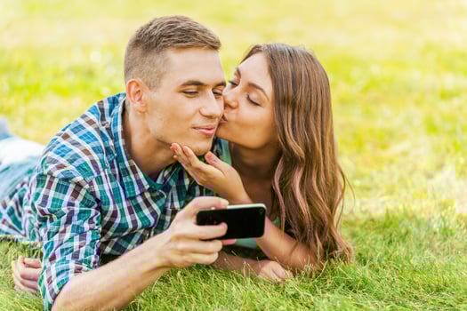 Taking picture of a kiss. Young couple lying on the grass and taking picture of themselves photo