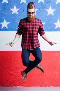 Having no equal. Handsome young bearded man in sunglasses jumping against American flag photo