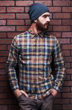 Handsome man in style. Handsome young bearded man holding hands in pockets and looking away while standing against brick wall photo