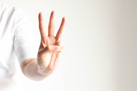 A hand showing number three by raising forefinger, middle finger and ring finger in close-up on white background and little light. photo