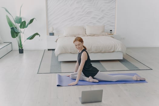 Red haired woman practicing yoga by video lessons in bedroom. Internet learning and home classes. photo