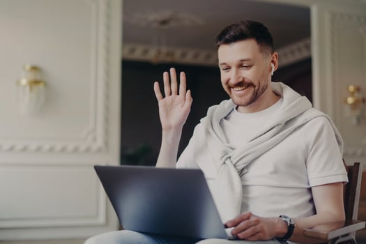 Portrait of businessman or freelancer greeting somebody via laptop while sitting on chair at home photo