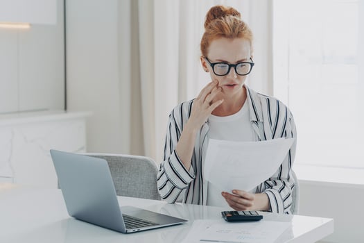 Young depressed woman with having financial problems, sitting at table with laptop and calculator photo