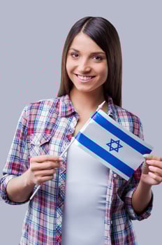 Beauty with Israeli flag. Happy young women holding flag of Israel while standing against grey background photo