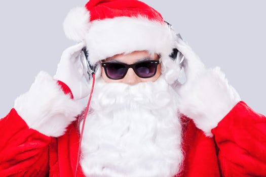 Cool Santa. Santa Claus in sunglasses adjusting his headphones while standing against grey background photo