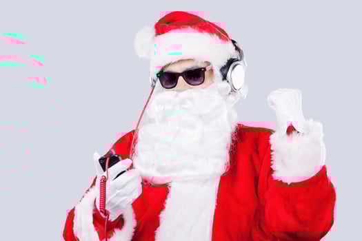 Enjoying Christmas music. Santa Claus in sunglasses and headphones listening to MP3 Player and gesturing while standing against grey background photo