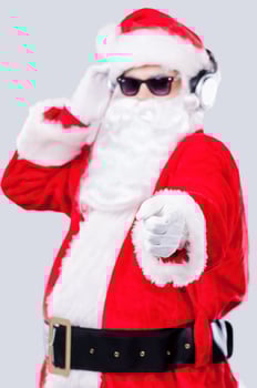 Merry Christmas to you Cool Santa Claus in sunglasses adjusting his headphones and pointing you while standing against grey background photo