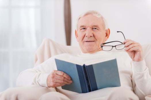 Reading his favorite book . Cheerful senior man reading a book while sitting in chair photo