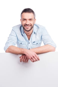 Your advertising below. Handsome young man in casual wear leaning at copy space and smiling while standing against white background photo