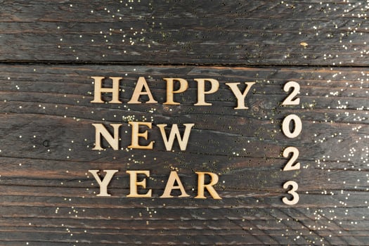 Happy New year 2023 celebration. Wooden text on wooden background with scattered golden confetti photo