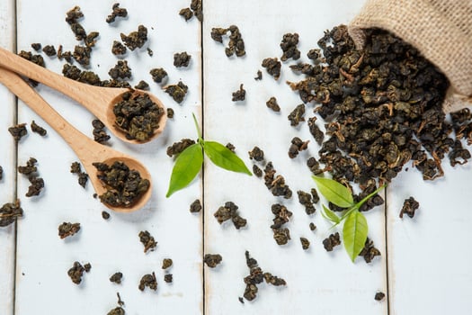 Dried tea with wooden spoon and sackcloth on white wooden photo