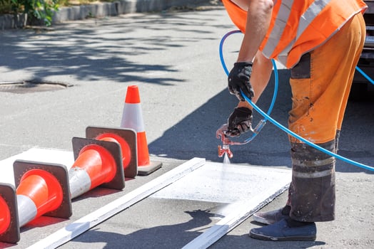 A road worker in orange overalls airbrushes white road markings of a pedestrian crossing on a sunny day. photo