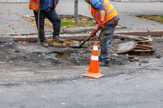 A team of road workers with a shovel and iron crowbar is repairing a sewer hatch on the roadway. photo