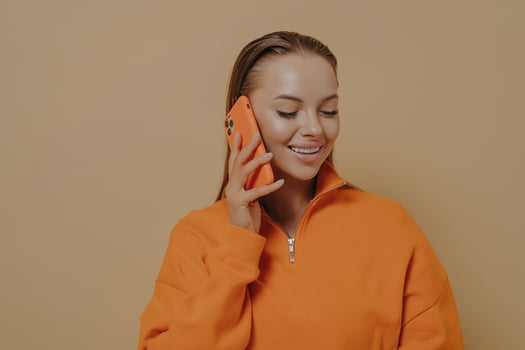 Happy young woman talking on mobile phone with friend, enjoying call conversation, isolated on beige photo