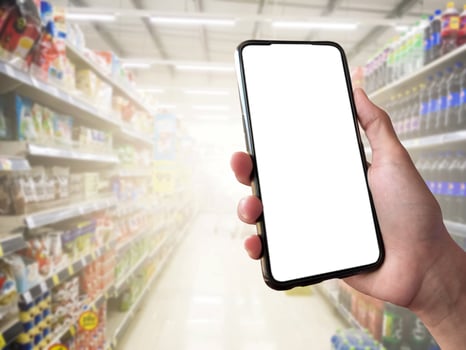 Smart shopping concept mobile phone in hand in front of goods shelves in supermarket and grocery store. blank white screen mockup for your own creativity. photo