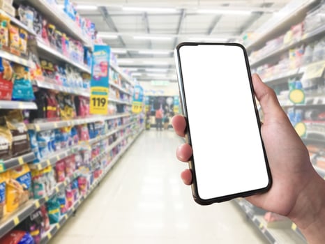 Smart shopping concept mobile phone in hand in front of goods shelves in supermarket and grocery store. blank white screen mockup for your own creativity. photo