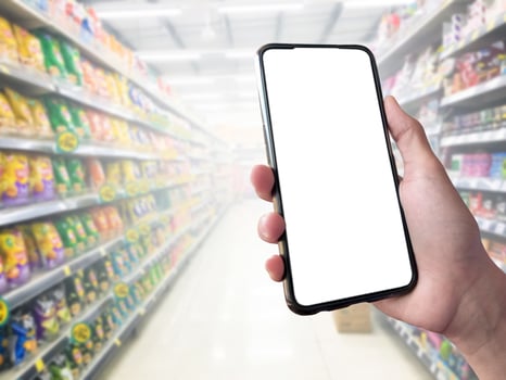 Smart shopping concept mobile phone in hand in front of goods shelves in supermarket and grocery store. blank white screen mockup for your own creativity. photo