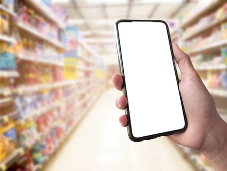 Smart shopping concept mobile phone in hand in front of goods shelves in supermarket and grocery store. blank white screen mockup for your own creativity. photo