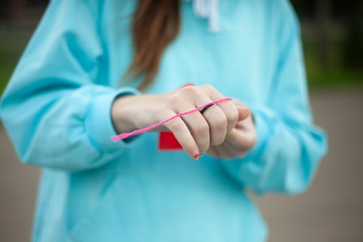 Child ties thread to heart. Girl holds red cardboard in her hands. Needlework on street. photo