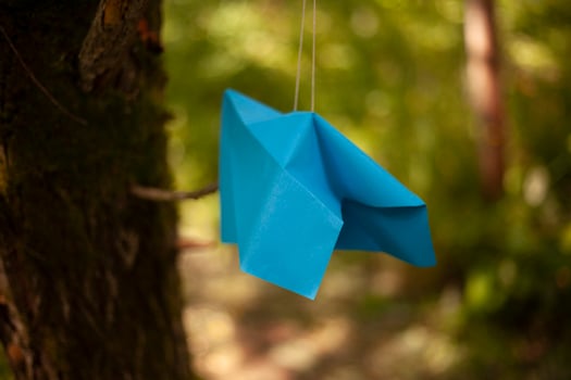 Paper airplane hangs on string. Origami made of blue paper. Decoration of park. photo