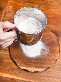 sifting the flour through sifter on wooden board photo