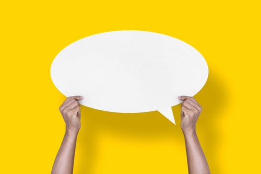 hand holding round white paper balloons speech bubbles isolated on yellow background photo