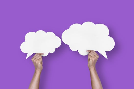 hand holding white paper cloud shape speech bubble balloon isolated on purple background communication bubbles photo