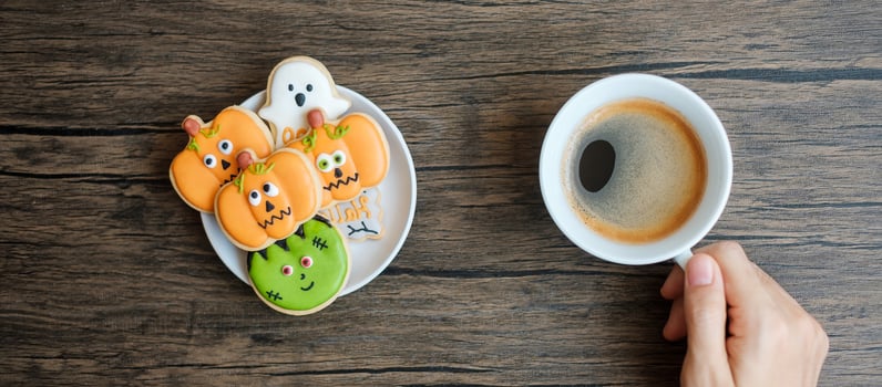 hand holding coffee cup during eating funny Halloween Cookies. Happy Halloween day, Trick or Threat, Hello October, fall autumn, Traditional, party and holiday concept photo