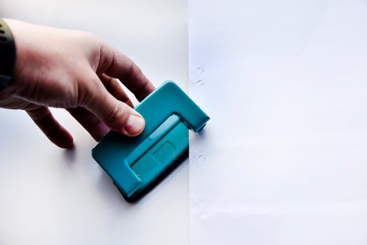 Green hole punch in hand on a white background. Stationery close-up. photo
