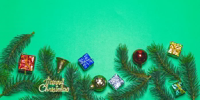 Top view of Christmas gift box red balls with spruce branches and bell on green background. photo