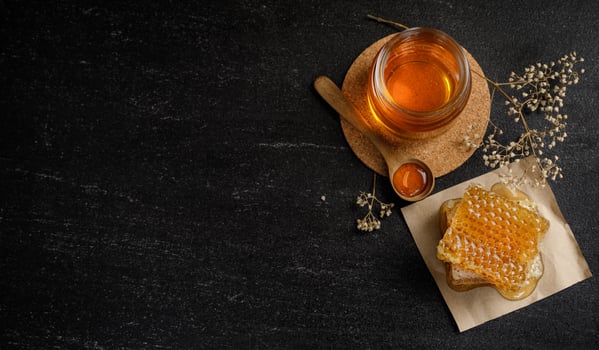 Honeycomb with honey dipper and dry flower on black background, bee products by organic natural ingredients concept photo