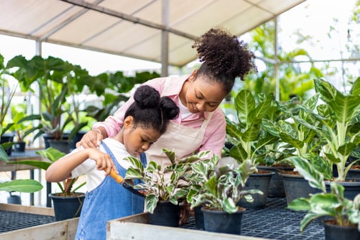African mother is teaching her daughter to grow ornamental houseplant using trowel to put organics compost in their own nursery garden center photo