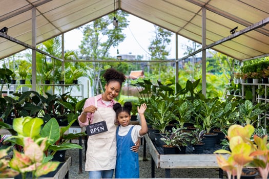African gardener and owner with her daughter is holding open sign in front of their ornamental houseplant at their own nursery garden center full of exotic and tropical plant concept photo
