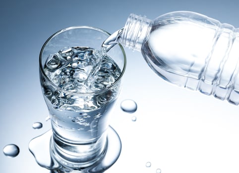 Pouring fresh pure water from bottle into a glass on the table with water drops, Healthcare and beauty hydration concept photo