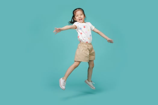 Playful energetic Asian little girl jumping in mid-air, empty space in studio shot isolated on colorful blue background photo