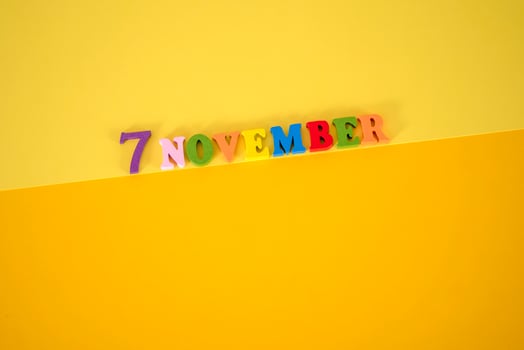 November 7 on a yellow, paper background with multicolored and wooden letters with space for text. photo