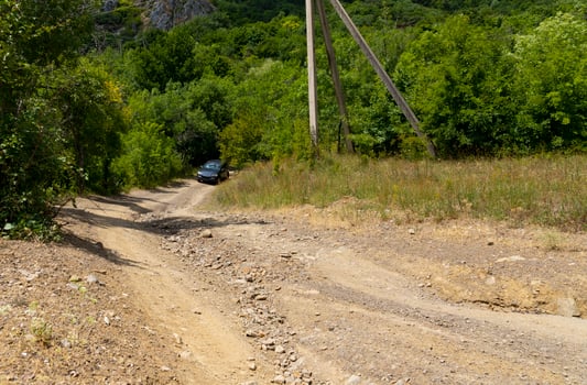 A muddy, country mountain road after rain with a large brown puddle and a small mountain river. photo