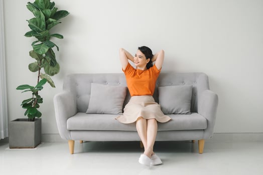 Peaceful young woman with hands behind head relaxing on cozy sofa at home photo